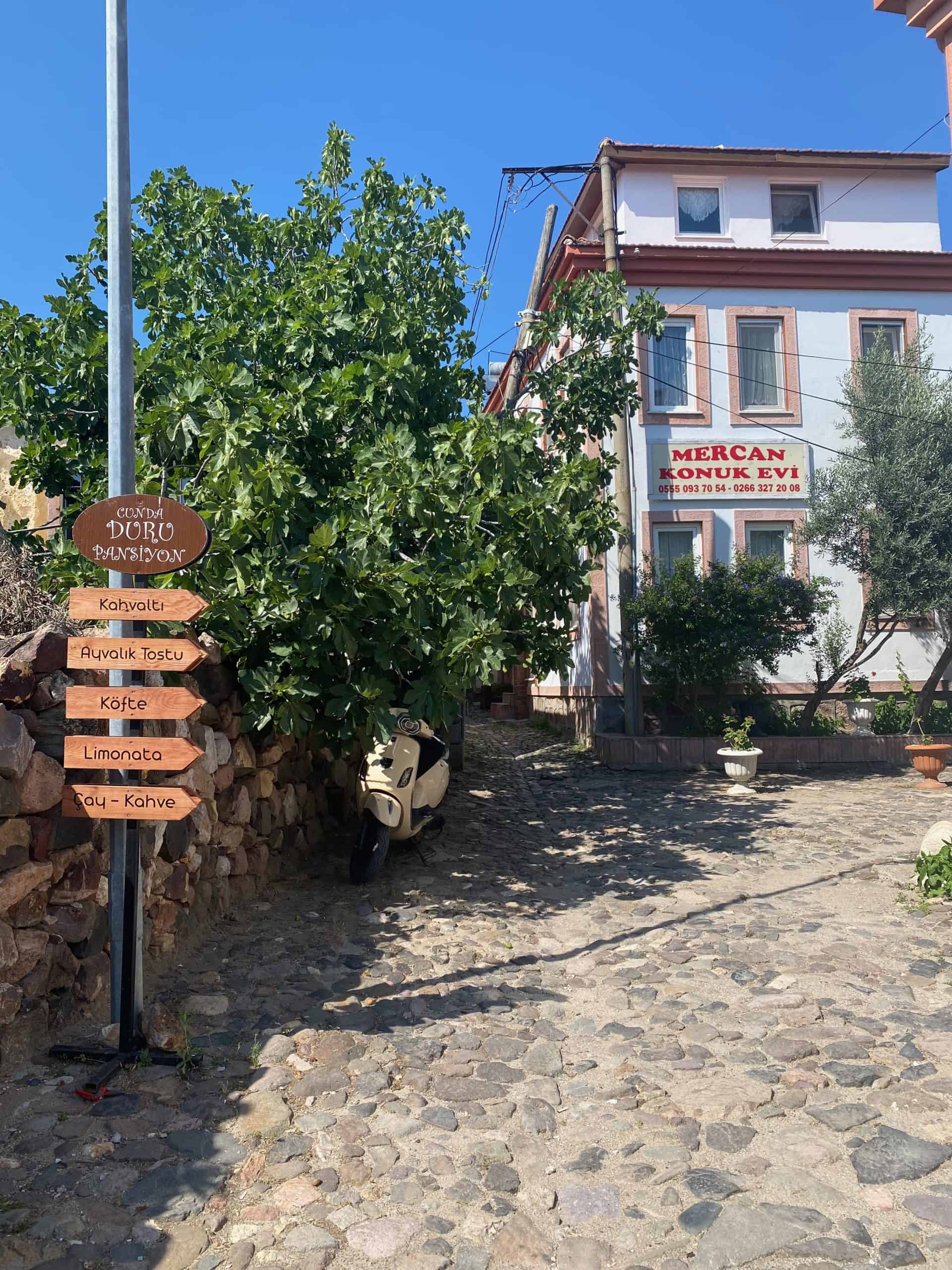 Charming street view on Cunda Island with a direction board, vespa and Greek-style home.