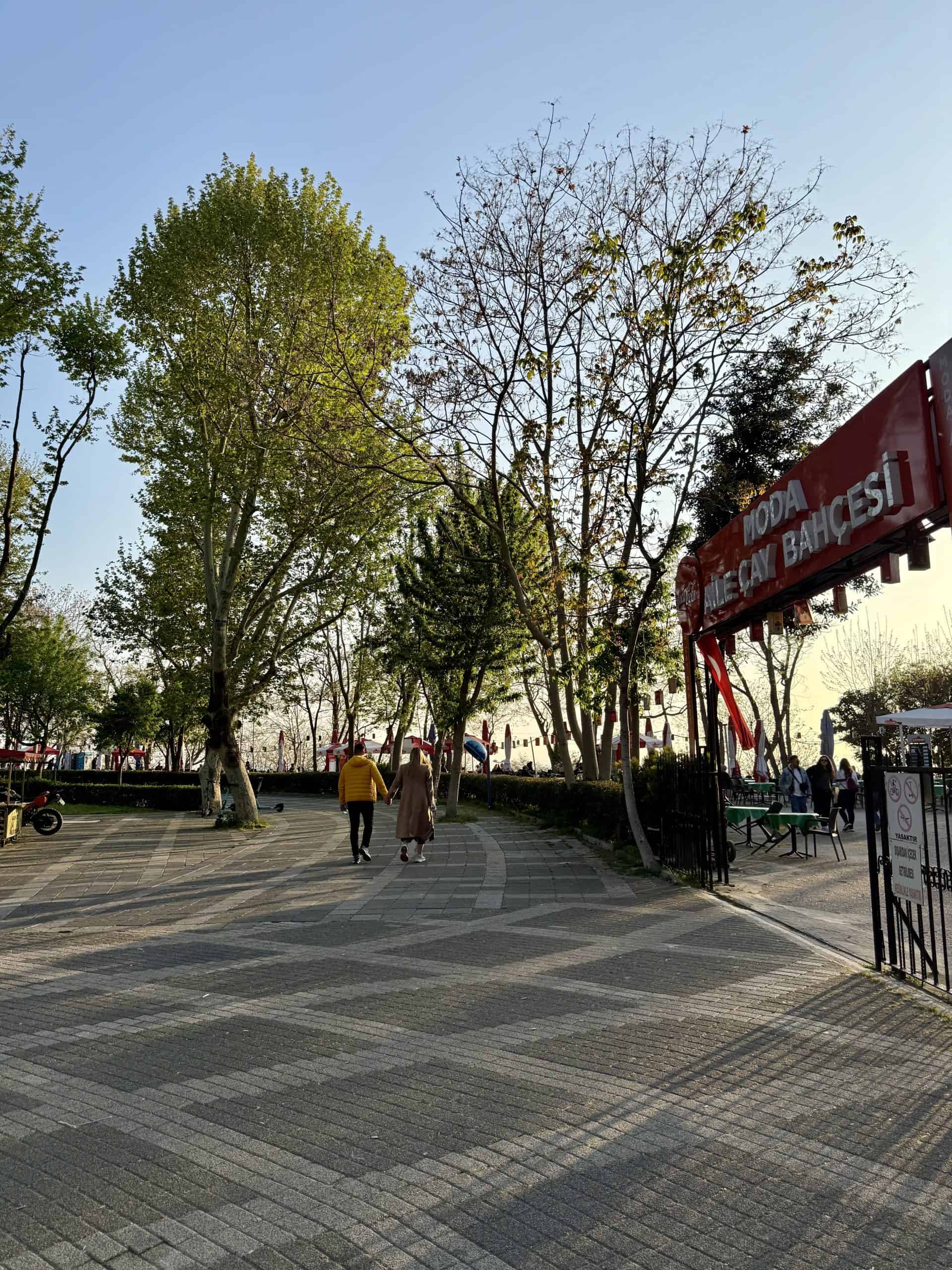 Couple walking down the street past the family tea garden in Moda, Istanbul