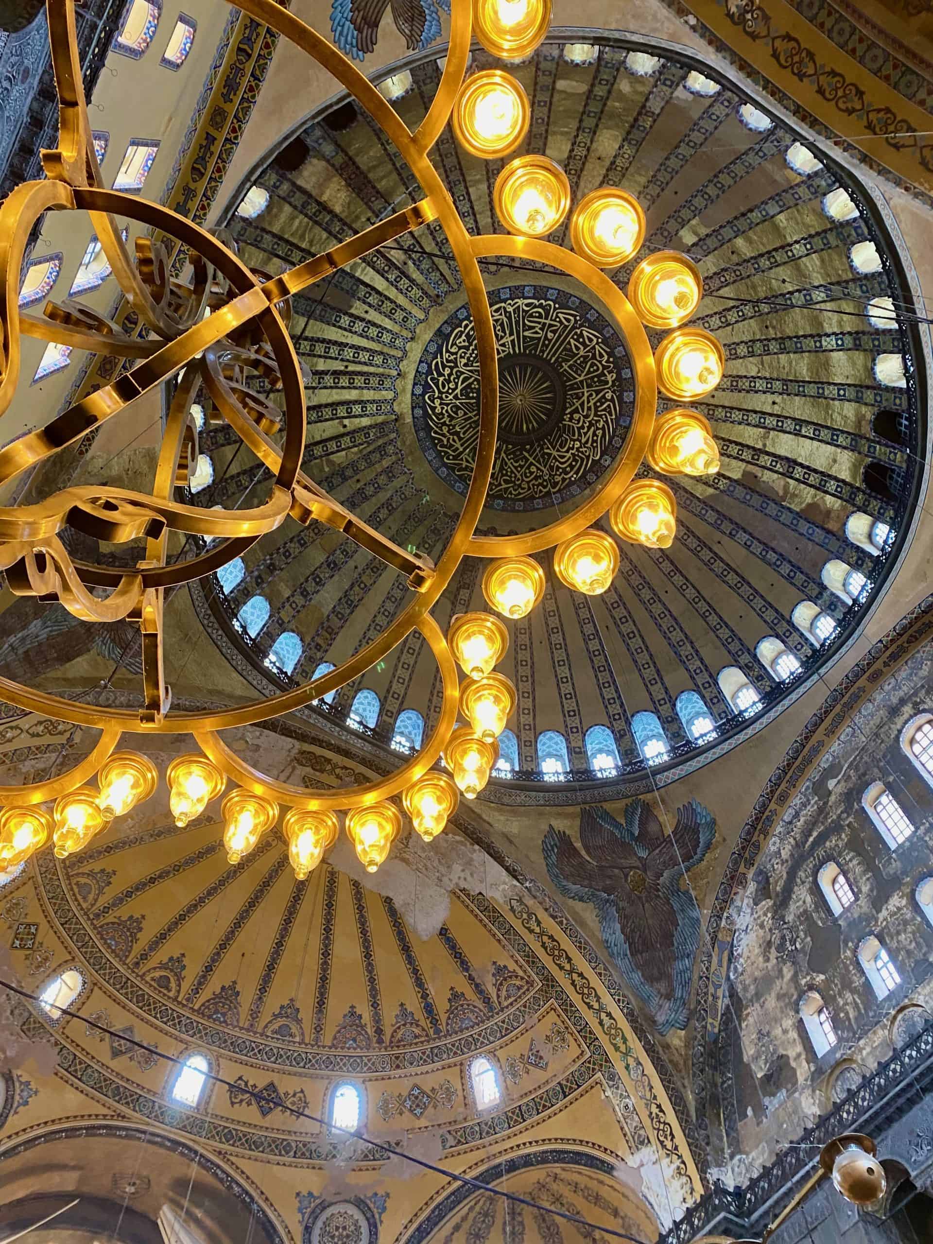 The ceiling of the Hagia Sophia featuring mosaics and beautiful low hanging light fixtures.